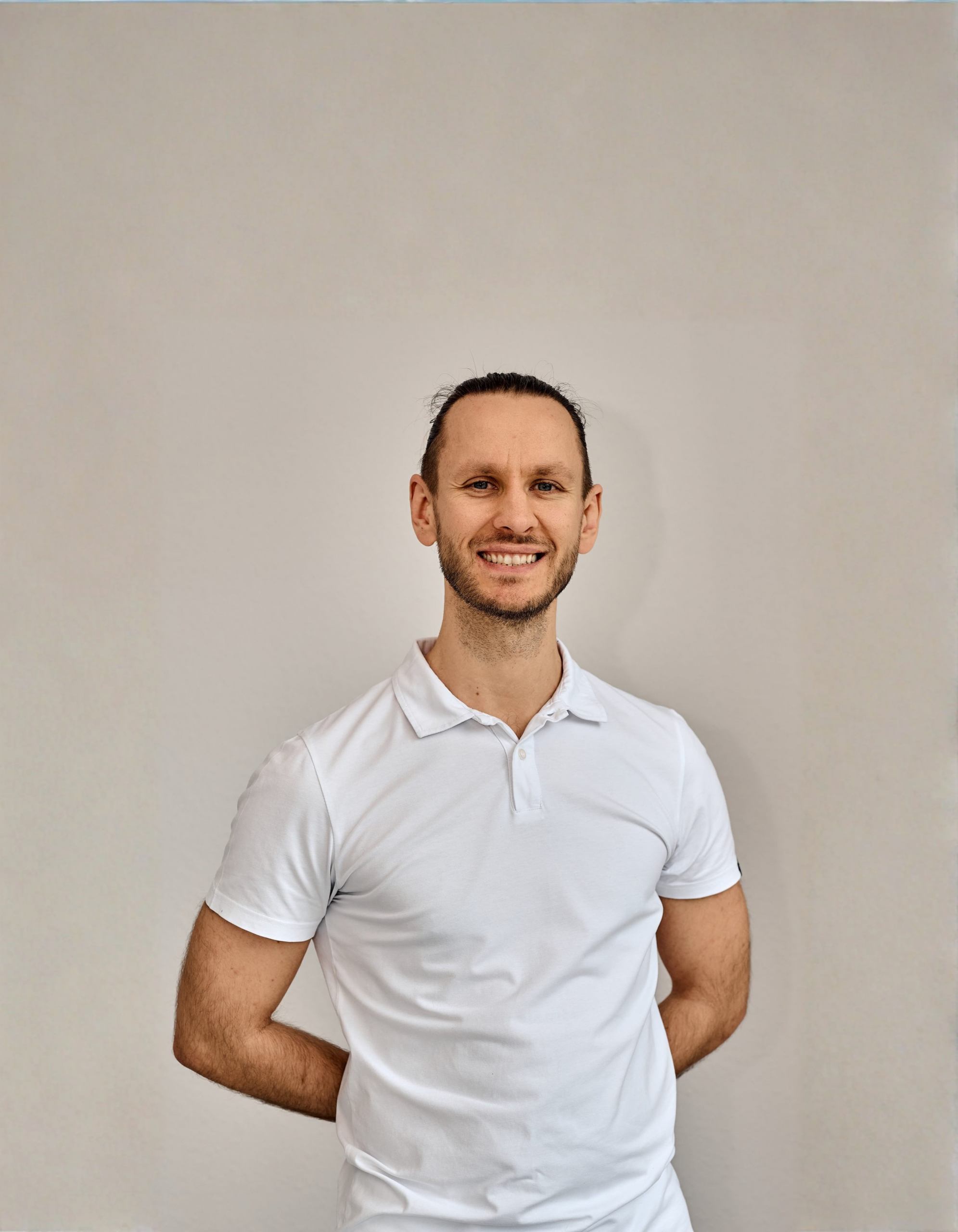 Porträt eines Physiotherapeuten der Praxis in Ostfildern in weißem Poloshirt vor neutralem Hintergrund.