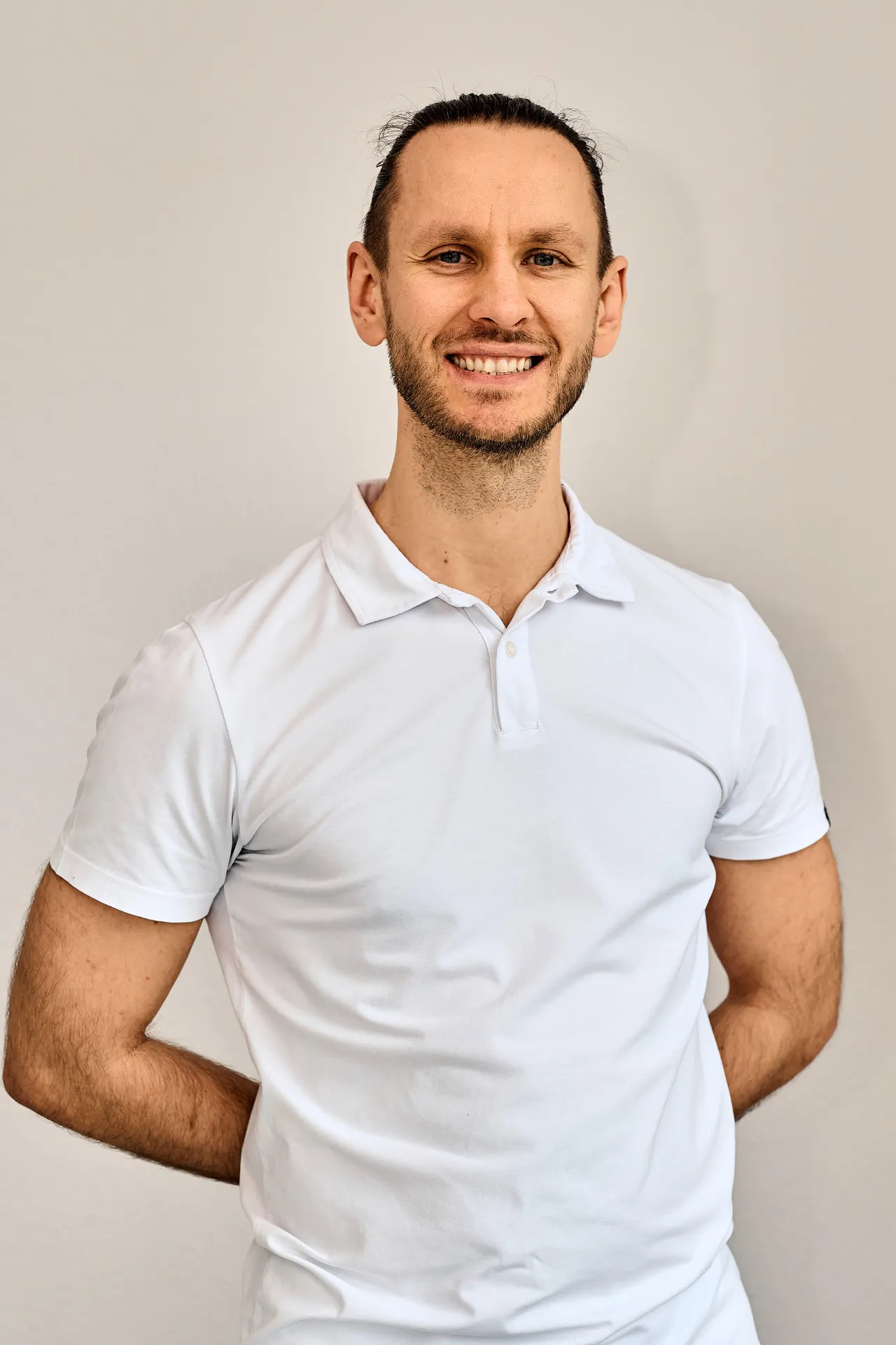 Porträt von Physiotherapeut Mateusz Karauda, Magister der Physiotherapie (PL), lächelnd in weißer Praxisbekleidung vor hellem Hintergrund – Privatpraxis Karauda Ostfildern.